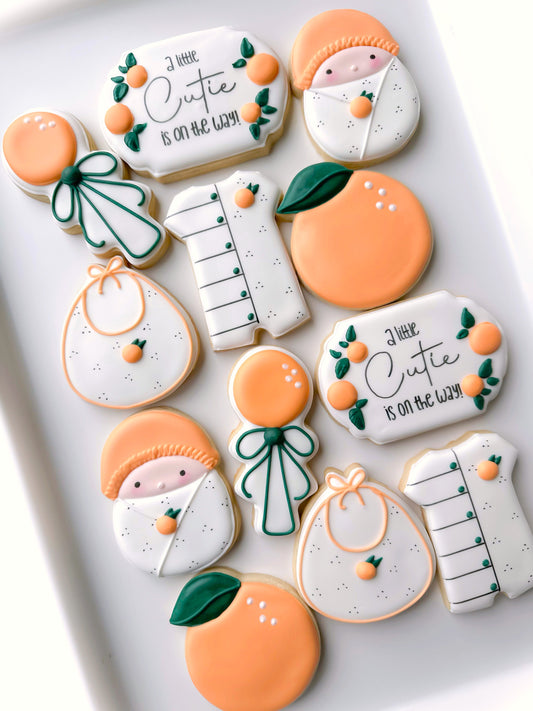 a little cutie on the way, orange rattle, bib, swaddled baby, romper, baby shower cookies