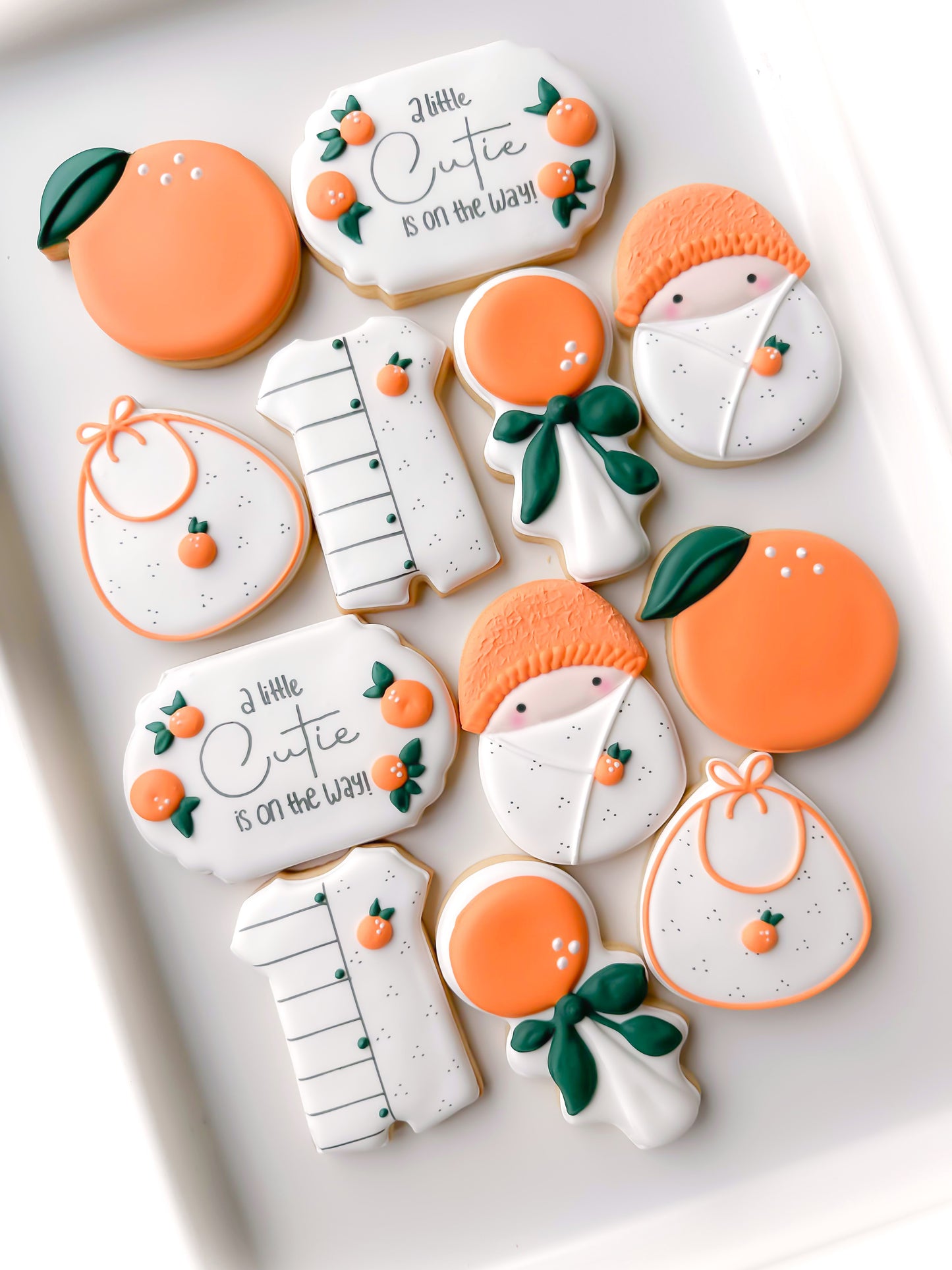 a little cutie on the way, orange rattle, bib, swaddled baby, romper, baby shower cookies